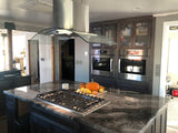 A modern kitchen with a marble island has an advanced control panel and gas stove, plus ProlineRangeHoods.com range hood.