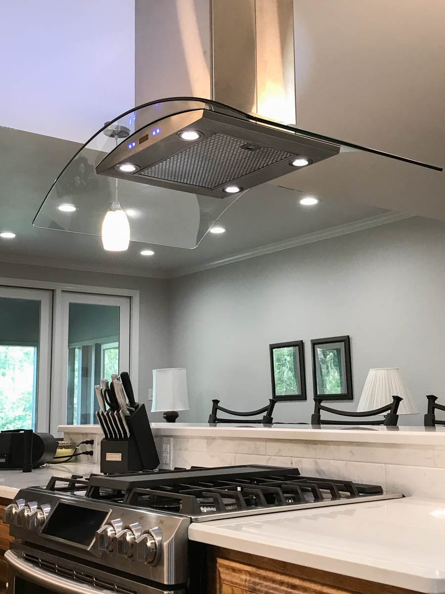 Stainless steel kitchen stove with a Proline PLFI 544 island range hood by ProlineRangeHoods.com, featuring an advanced control panel, knife set, and decorative items on the counter.