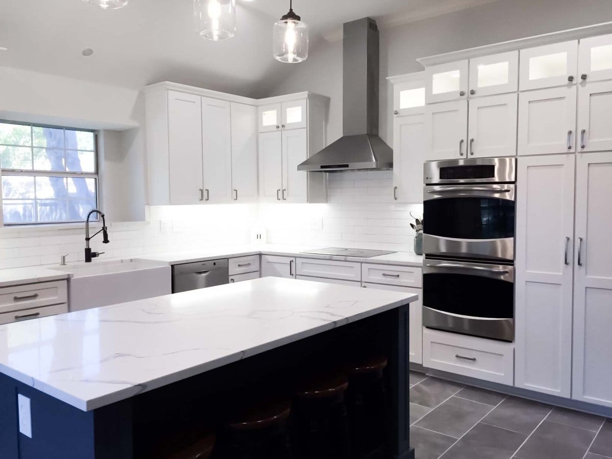 Modern kitchen with white cabinets, stainless steel appliances, a ProlineRangeHoods.com PLFW 129E hood, marble island, and lights.