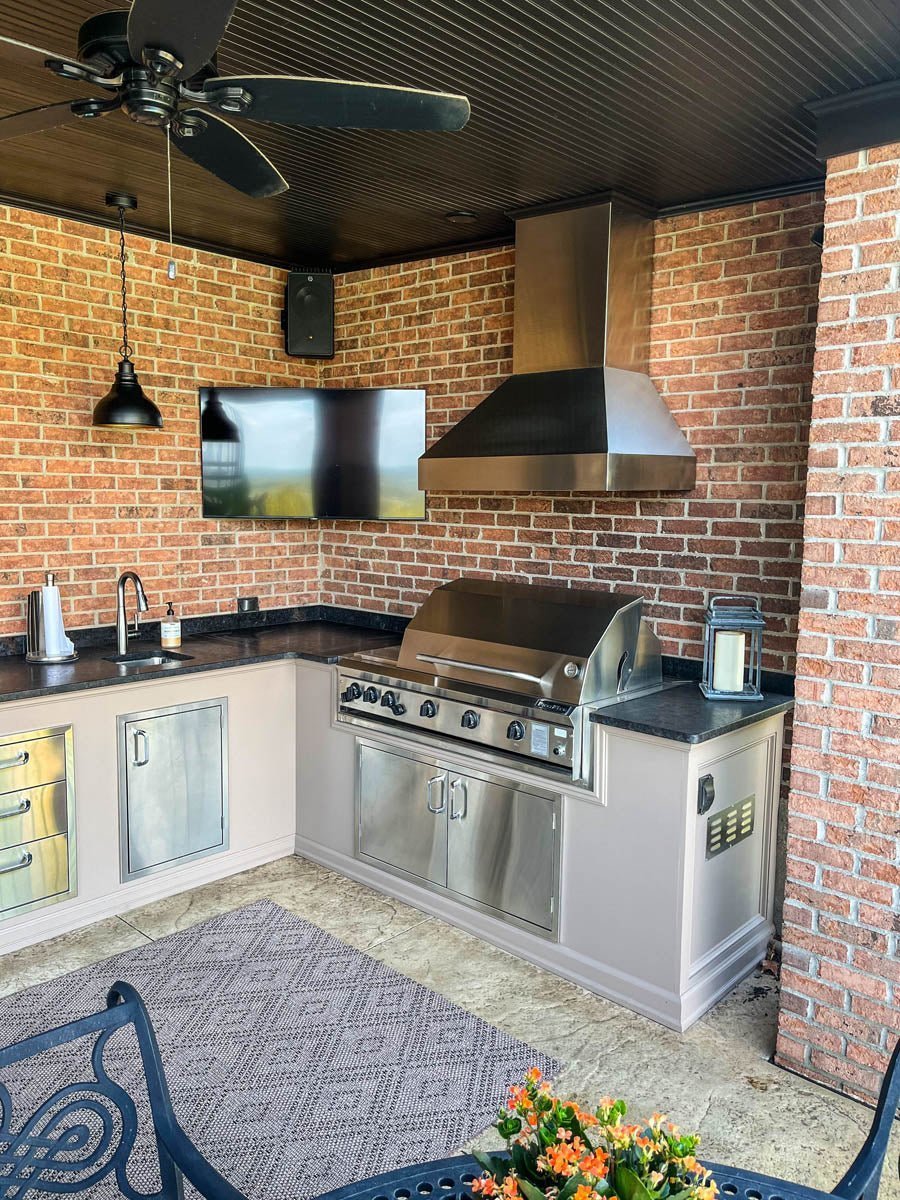 Outdoor kitchen with grill, TV, sink, cabinets, and ProlineRangeHoods.com wall hood with variable CFM, ducted design.