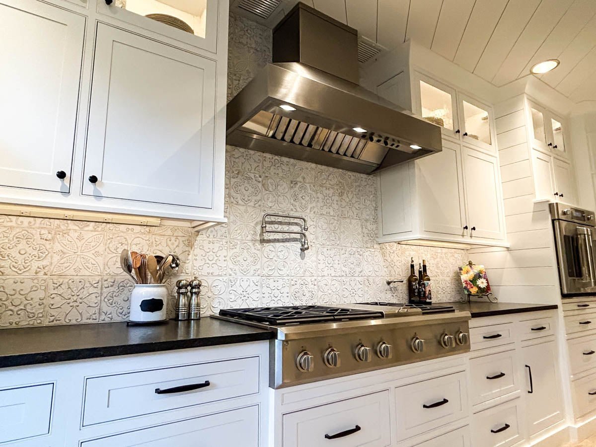Modern kitchen with white cabinets, patterned backsplash, and a ProlineRangeHoods.com wall-mounted hood in stainless steel.