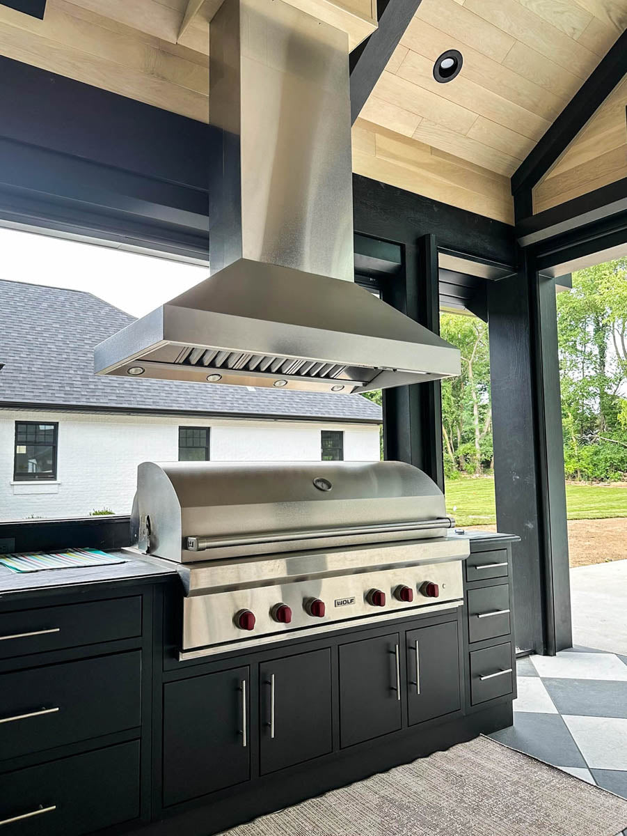 Outdoor kitchen with ProlineRangeHoods.com ProVI Island Hood in stainless steel, sleek black cabinets, wooden ceiling.
