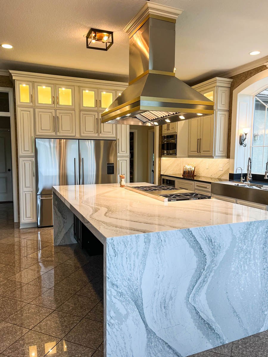 This stylish kitchen features a marble island, stainless appliances, and a ProlineRangeHoods.com Island Range Hood.