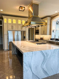 This stylish kitchen features a marble island, stainless appliances, and a ProlineRangeHoods.com Island Range Hood.