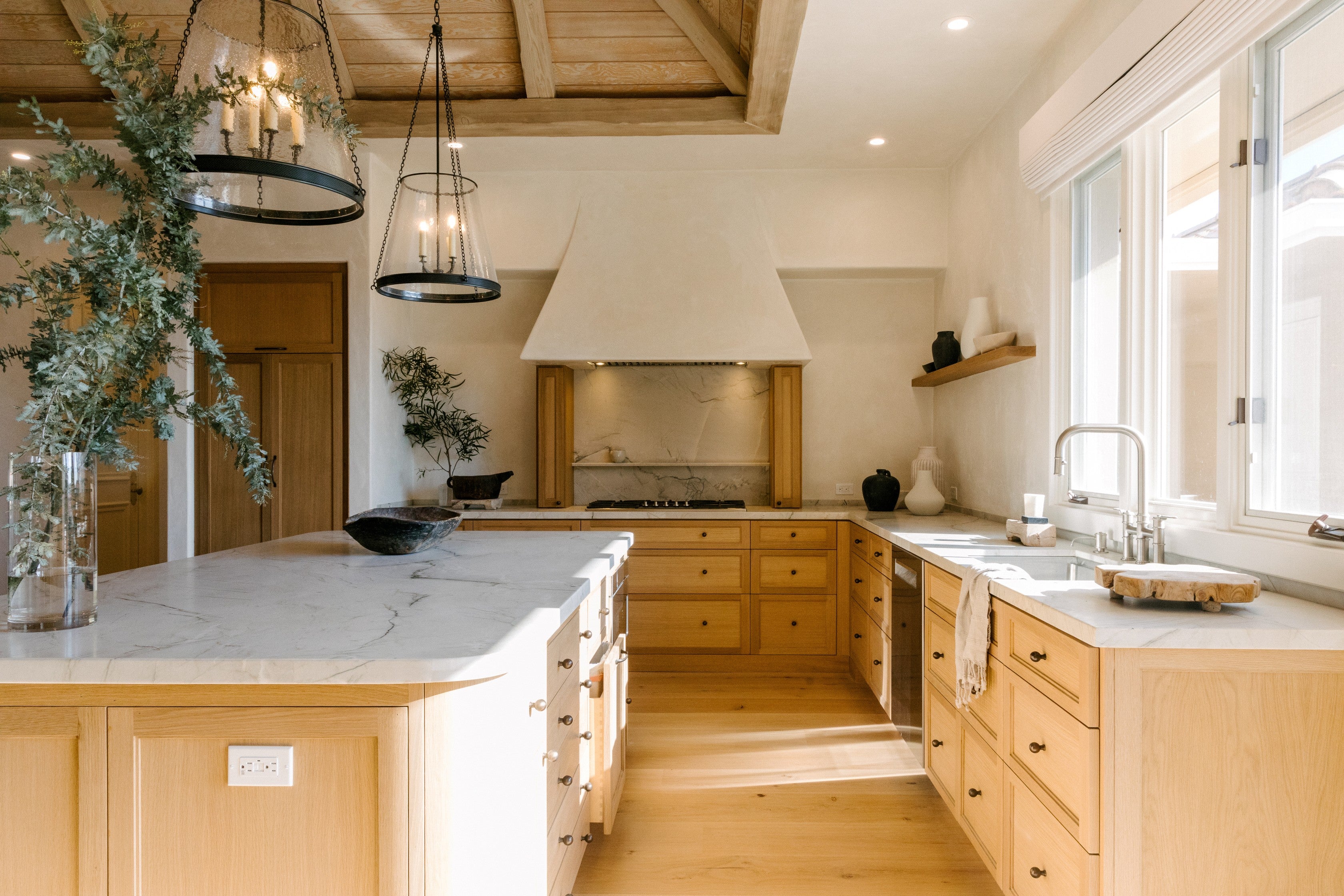 Modern kitchen with wooden cabinets, white countertops, and large windows.