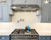Stainless steel gas stove, ProlineRangeHoods.com range hood, pot filler, and blue-gray cabinets in a modern kitchen.