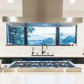 Modern kitchen with large stovetop, sink, wide window overlooking trees—scenic view. ProlineRangeHoods.com.