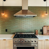 Modern kitchen with stainless steel stove, green tile backsplash, and pendant lights. ProlineRangeHoods.com.