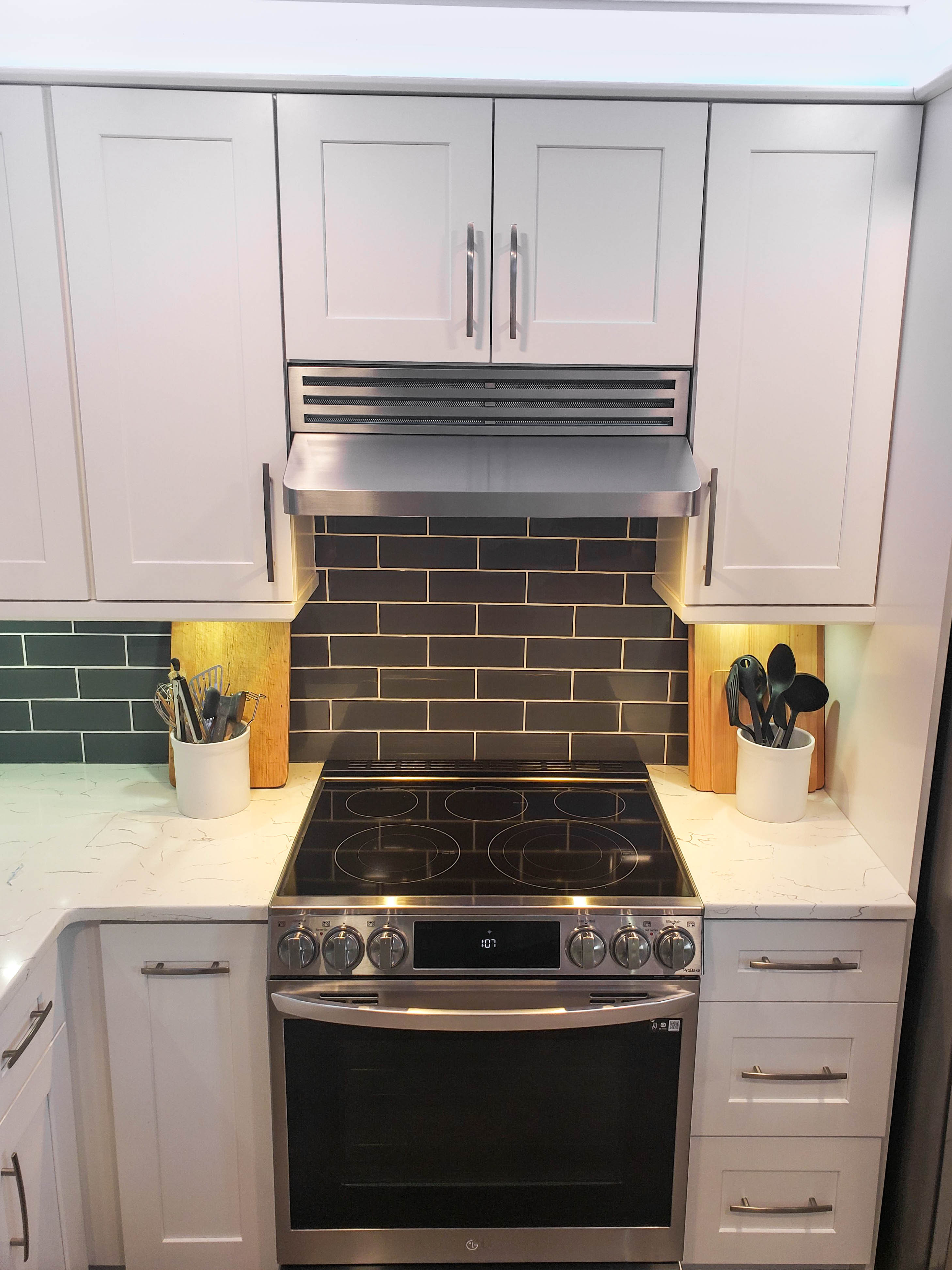 Modern kitchen with white cabinets, stainless steel oven, black tile backsplash; featuring a Proline PLJW 185 Range Hood by ProlineRangeHoods.com.