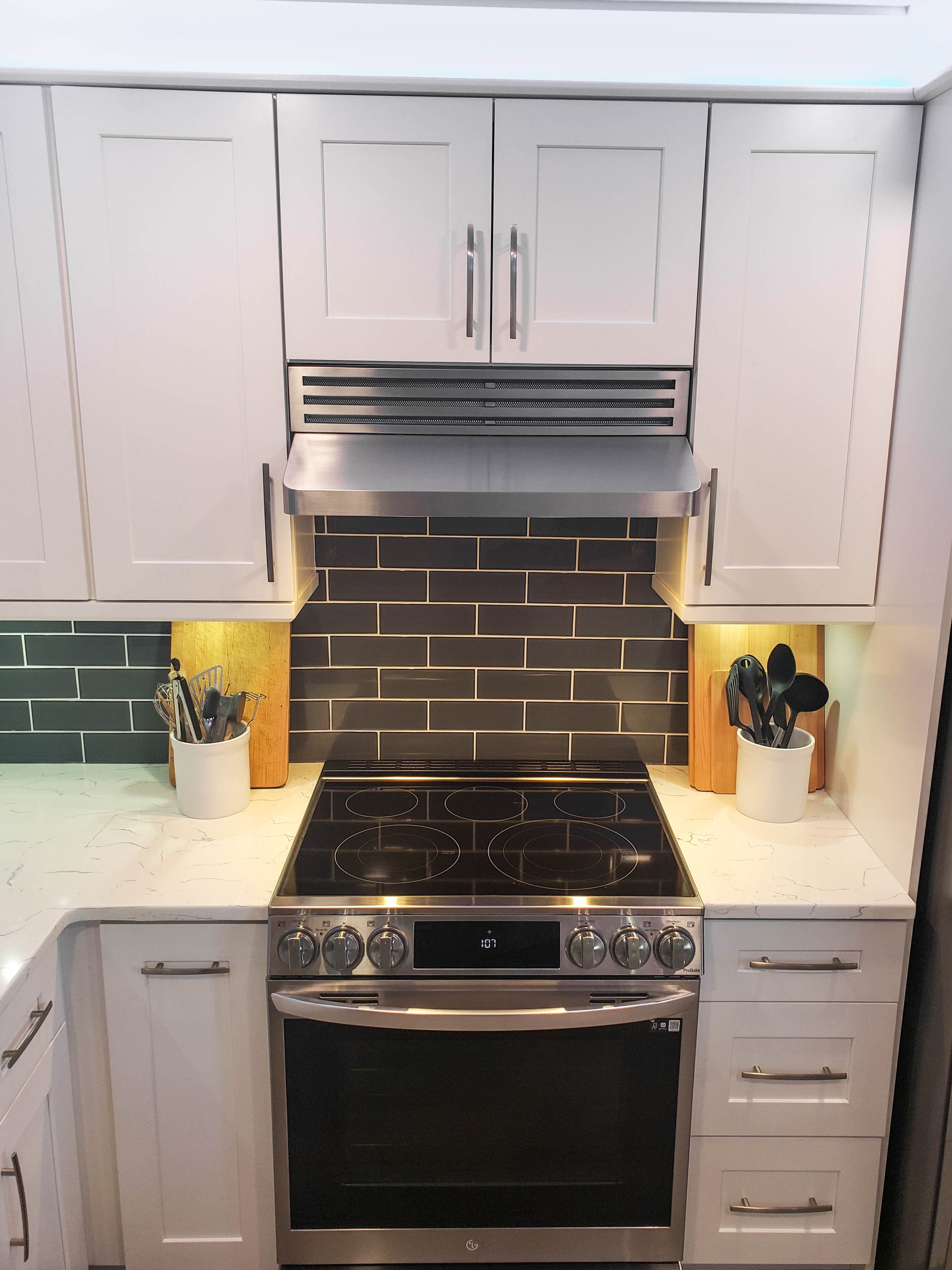 Modern kitchen with white cabinets, stainless steel oven, black tile backsplash; featuring a Proline PLJW 185 Range Hood by ProlineRangeHoods.com.