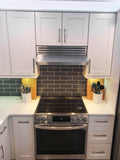 Modern kitchen with white cabinets, stainless steel oven, black tile backsplash; featuring a Proline PLJW 185 Range Hood by ProlineRangeHoods.com.