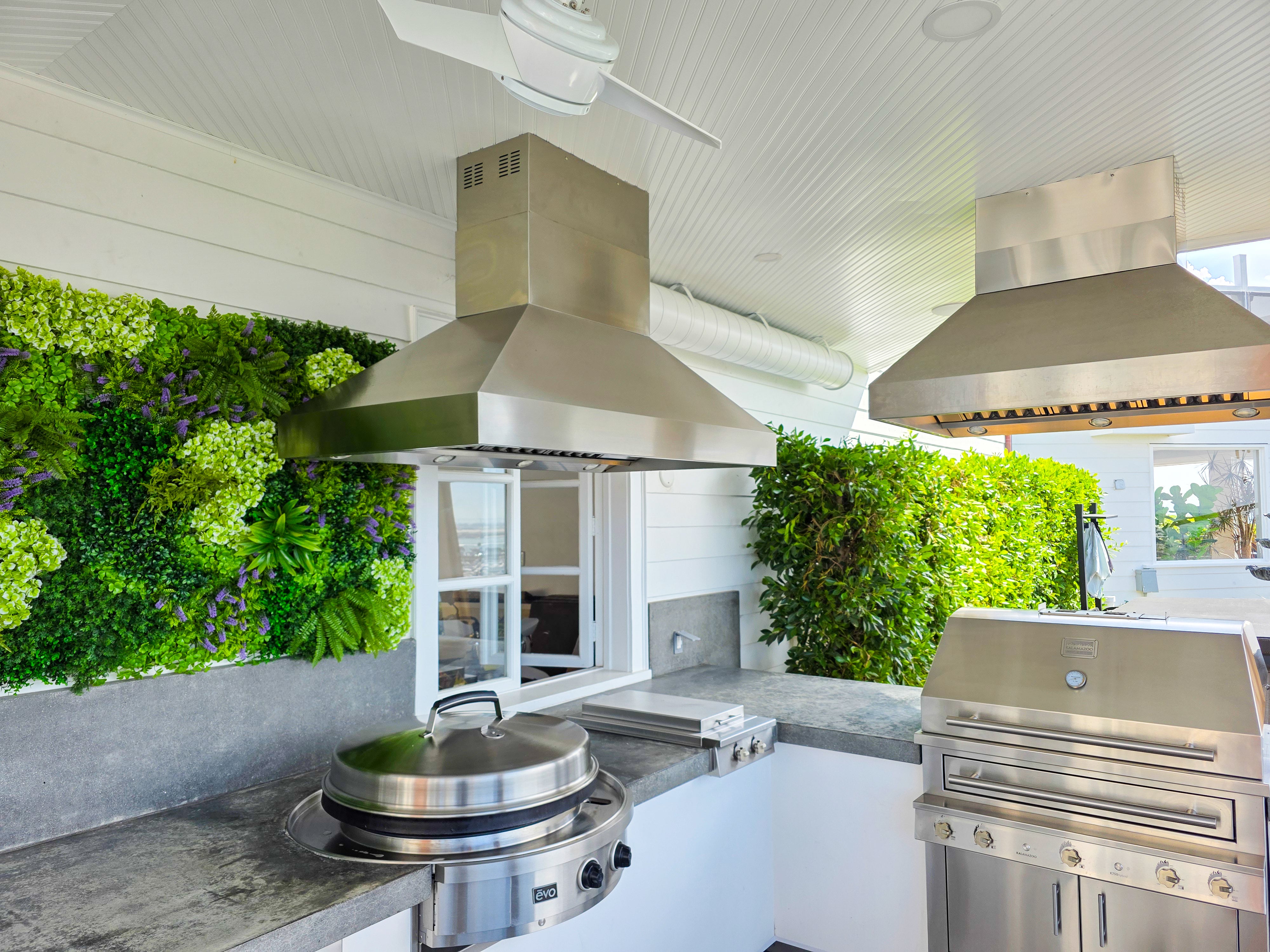 Two PLGI BBQ Ultra Island range hoods from ProlineRangeHoods.com over an outdoor kitchen with grill and cooktop.