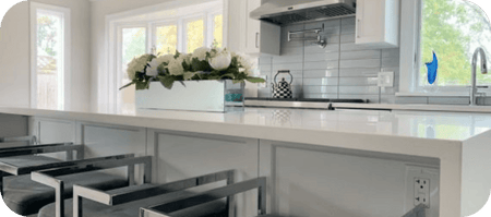 Modern white kitchen with metal bar stools, flowers, large sunny windows. ProlineRangeHoods.com.