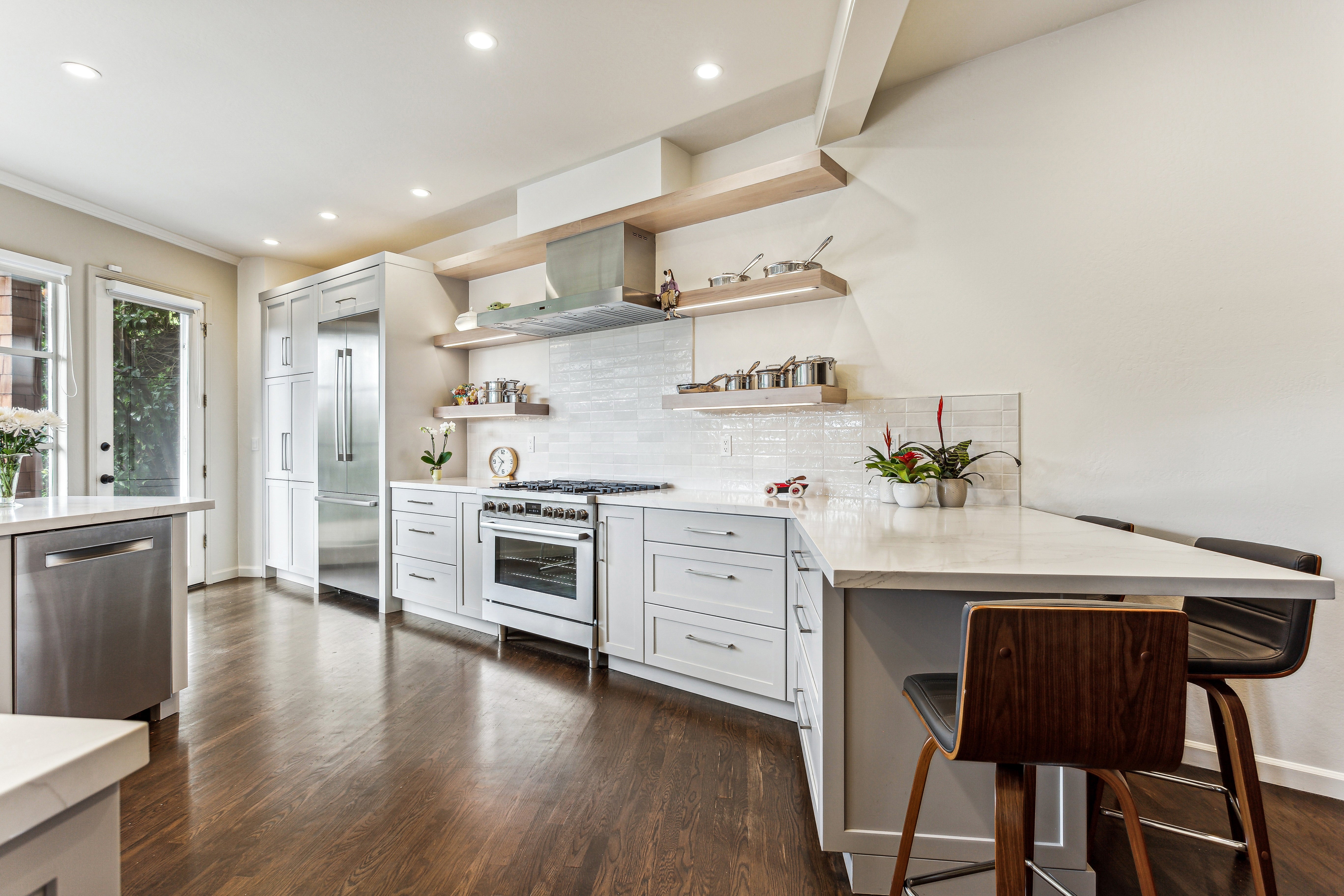 Modern kitchen with white cabinets, stainless steel appliances, and wooden flooring.