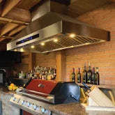 Stainless steel range hood with lights over grill, countertop, and utensils; ProlineRangeHoods.com in background.