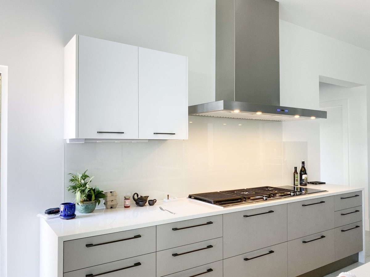 Stylish kitchen with white cabinets, ProlineRangeHoods.com wall-mounted range hood, 900/1100 CFM, plus plants and bottles.