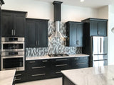 The modern kitchen showcases black cabinets, silver appliances, a marble countertop, and a geometric tile backsplash. The Proline Vector from ProlineRangeHoods.com provides efficient 600 CFM ventilation in sleek stainless steel and black.