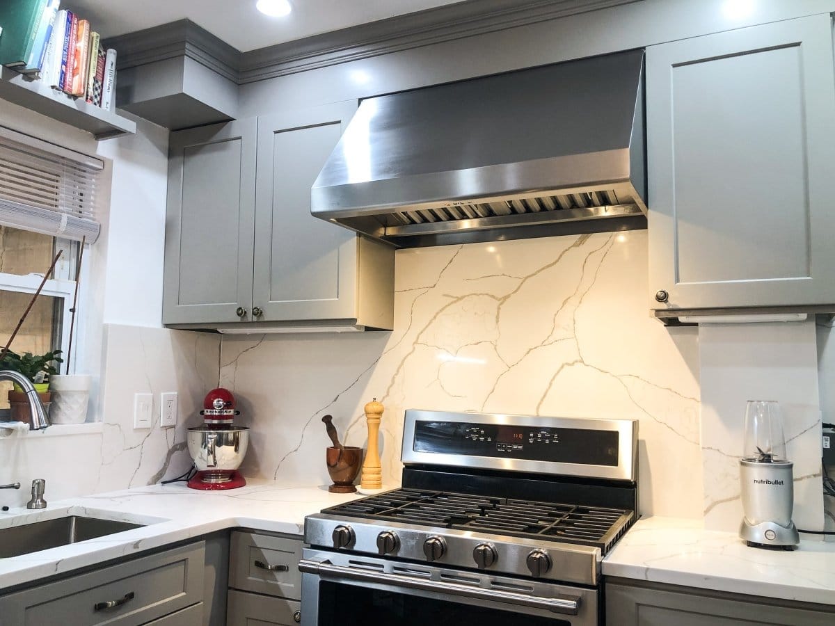 Contemporary kitchen with gray cabinets, ProlineRangeHoods.com stainless PLJW 108 range hood, marble backsplash.