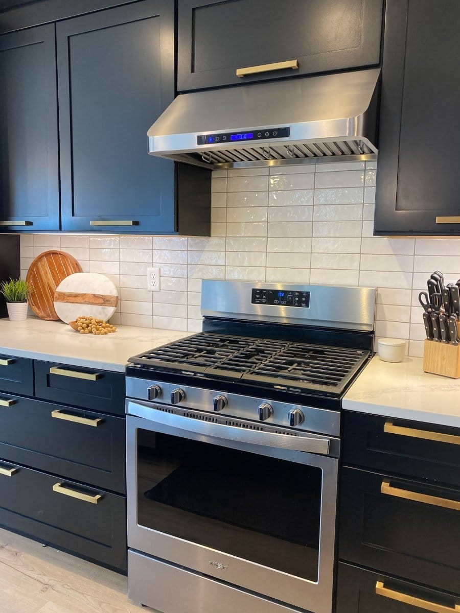 The modern kitchen showcases a sleek stainless steel PLJW 113 vent hood by ProlineRangeHoods.com, with black cabinets.