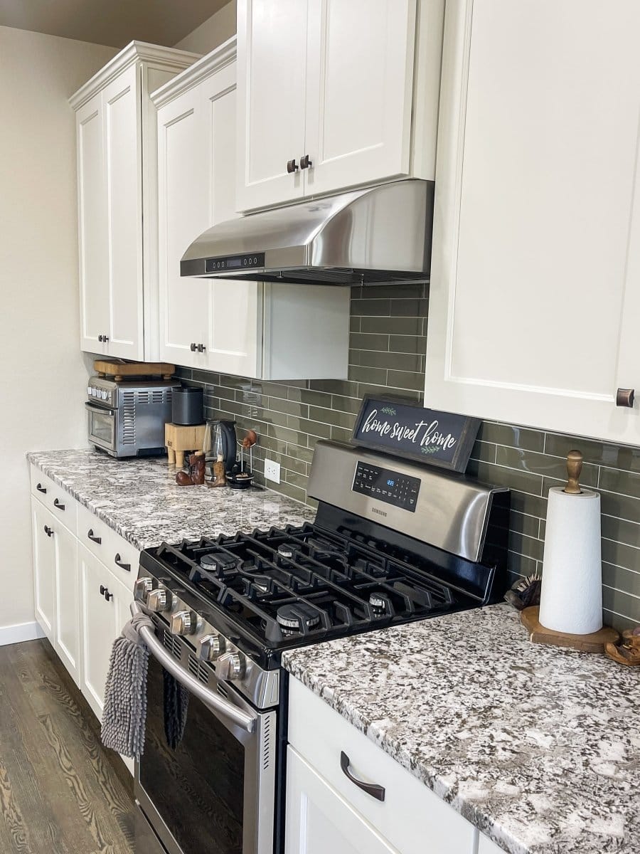 Modern kitchen with white cabinets, granite counters, a stainless stove & ProlineRangeHoods.com 900 CFM under-cabinet hood.