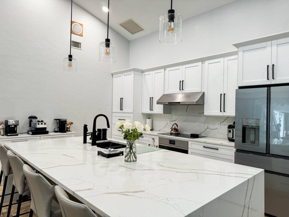 Contemporary kitchen with white cabinets, a ProlineRangeHoods.com PLJW 120 under cabinet hood, marble island, and pendant lights.