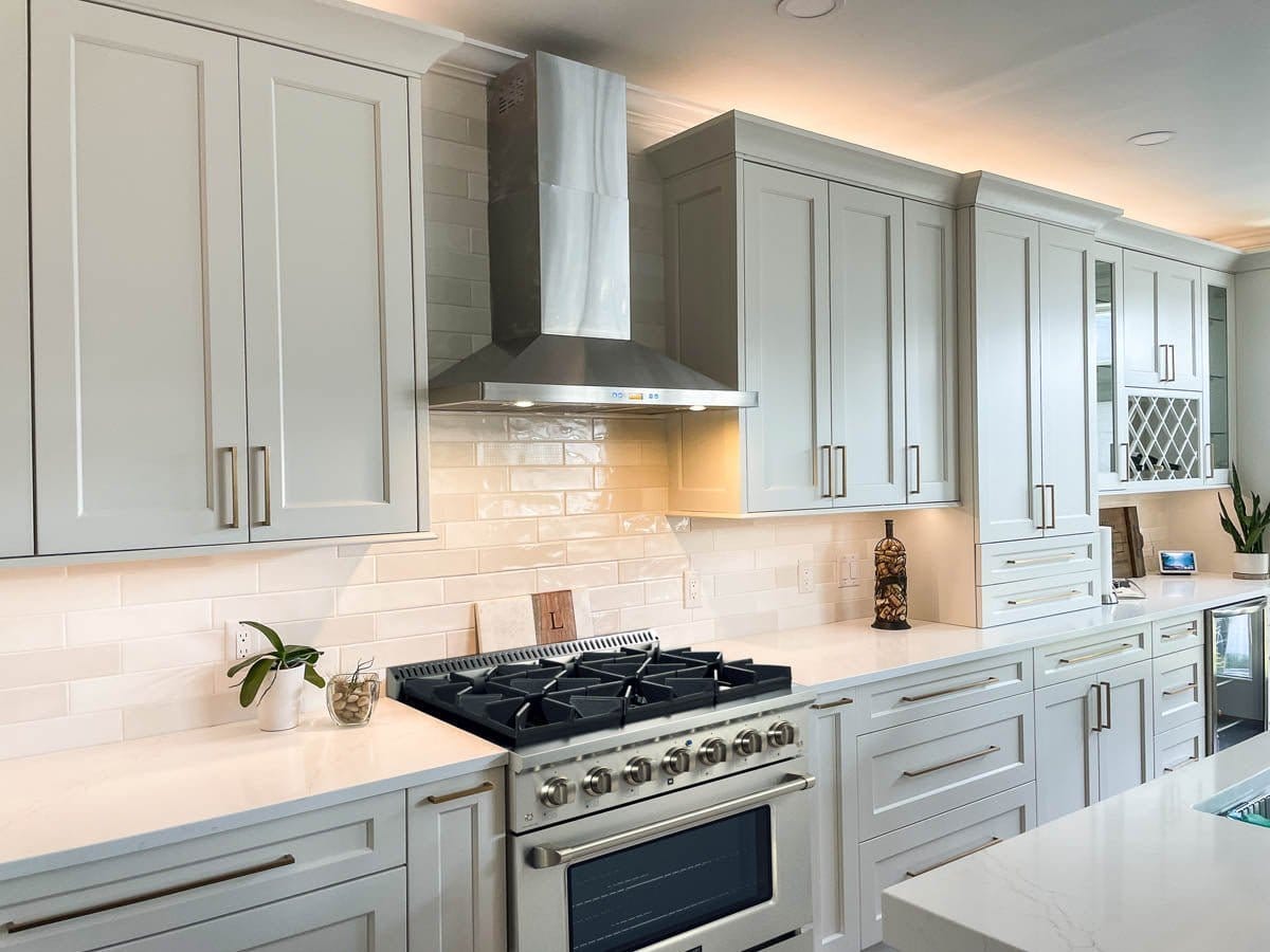 The contemporary kitchen with light cabinetry, ProlineRangeHoods.com's range hood, and white countertops offers dual fuel versatility.