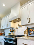 Bright kitchen with white cabinets, gold hardware, gas stove, ProlineRangeHoods.com Insert (600 CFM), and flowers.