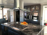 A modern kitchen with a marble island has an advanced control panel and gas stove, plus ProlineRangeHoods.com range hood.
