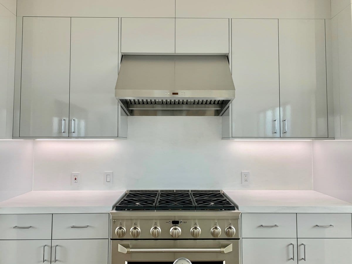 Modern kitchen with white cabinets, a Proline PLFW 832 range hood from ProlineRangeHoods.com offering low noise and lighting.