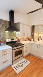 A modern kitchen with a Proline Vector hood from ProlineRangeHoods.com, tile backsplash, white cabinets, and a "HOME" mat.