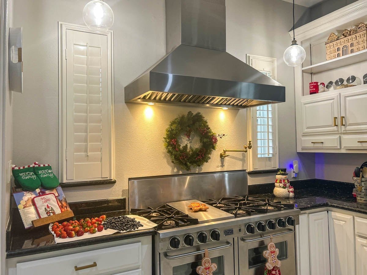 A festive kitchen features a wreath, cookies baking, holiday decor, and a ProlineRangeHoods.com stainless steel range hood.
