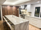 A contemporary kitchen with marble island, bar stools, wooden cabinets, stainless steel appliances, and ProlineRangeHoods.com.