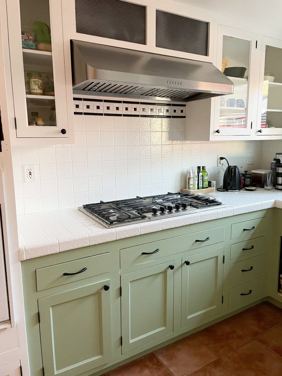 A kitchen featuring a gas stove, green cabinets, white tile backsplash, and the Proline PLJW 121 Hood from ProlineRangeHoods.com.