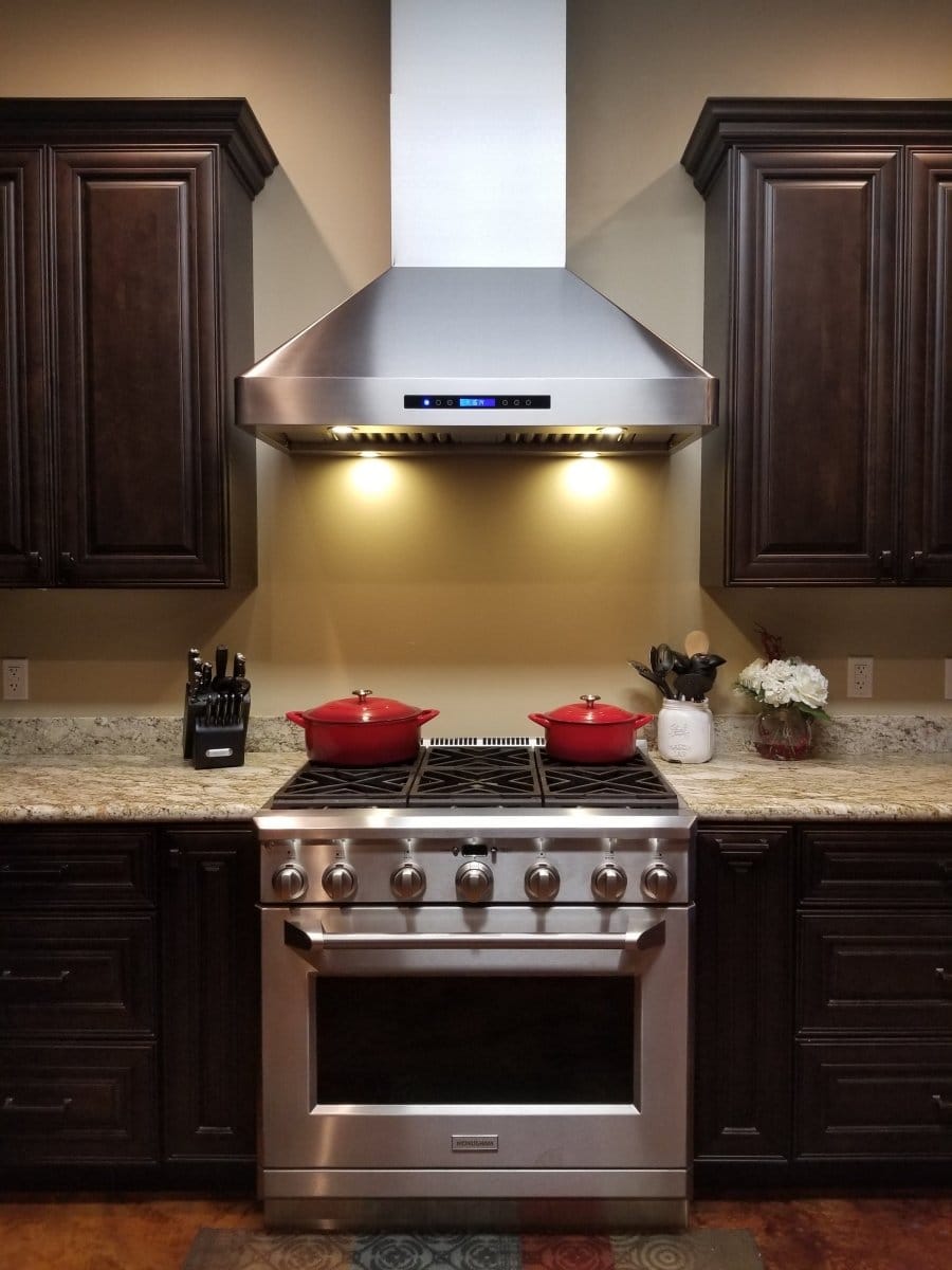 A modern kitchen featuring a stainless steel stove, dark cabinets, and the Proline PLJW 130 Hood from ProlineRangeHoods.com.