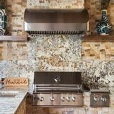Outdoor stainless steel grill and vent hood with stone backsplash, vases on shelves. ProlineRangeHoods.com.