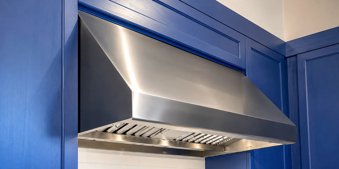 Stainless steel kitchen range hood installed under blue cabinets