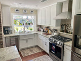 Modern kitchen with white cabinets, stainless appliances, farmhouse sink, potted plants. See ProlineRangeHoods.com.