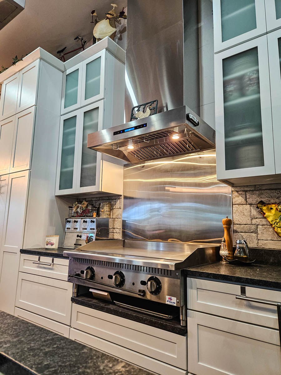 Modern kitchen with a ProlineRangeHoods.com PLFW 755 Range Hood, stainless stove, white cabinets, and black countertops.