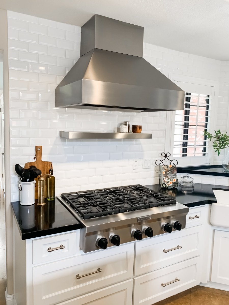 A modern kitchen with a sleek ProlineRangeHoods.com 54" and 60" stainless steel wall range hood, gas stove, and white cabinets.