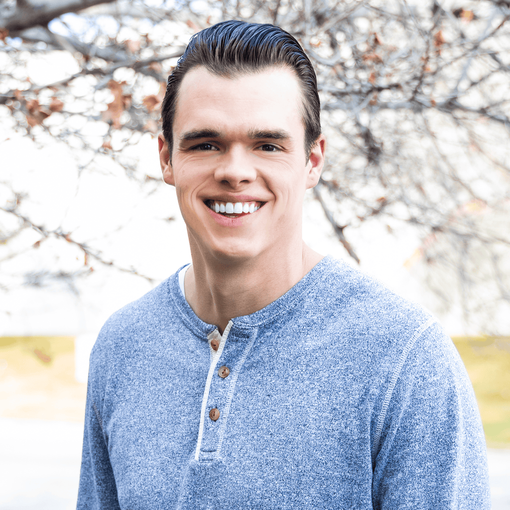 Smiling young man in a gray henley shirt outside by leafless branches, ProlineRangeHoods.com.