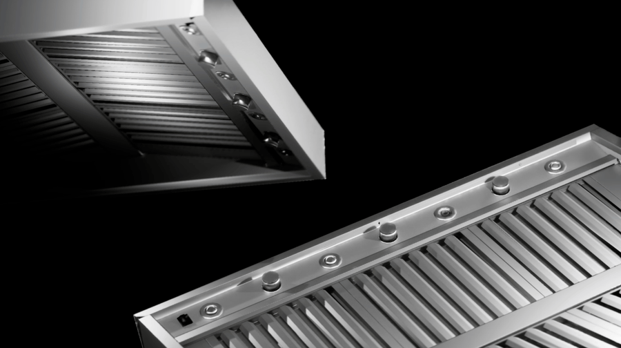 Close-up of two stainless steel range hoods with vent slats and controls, black background. ProlineRangeHoods.com.