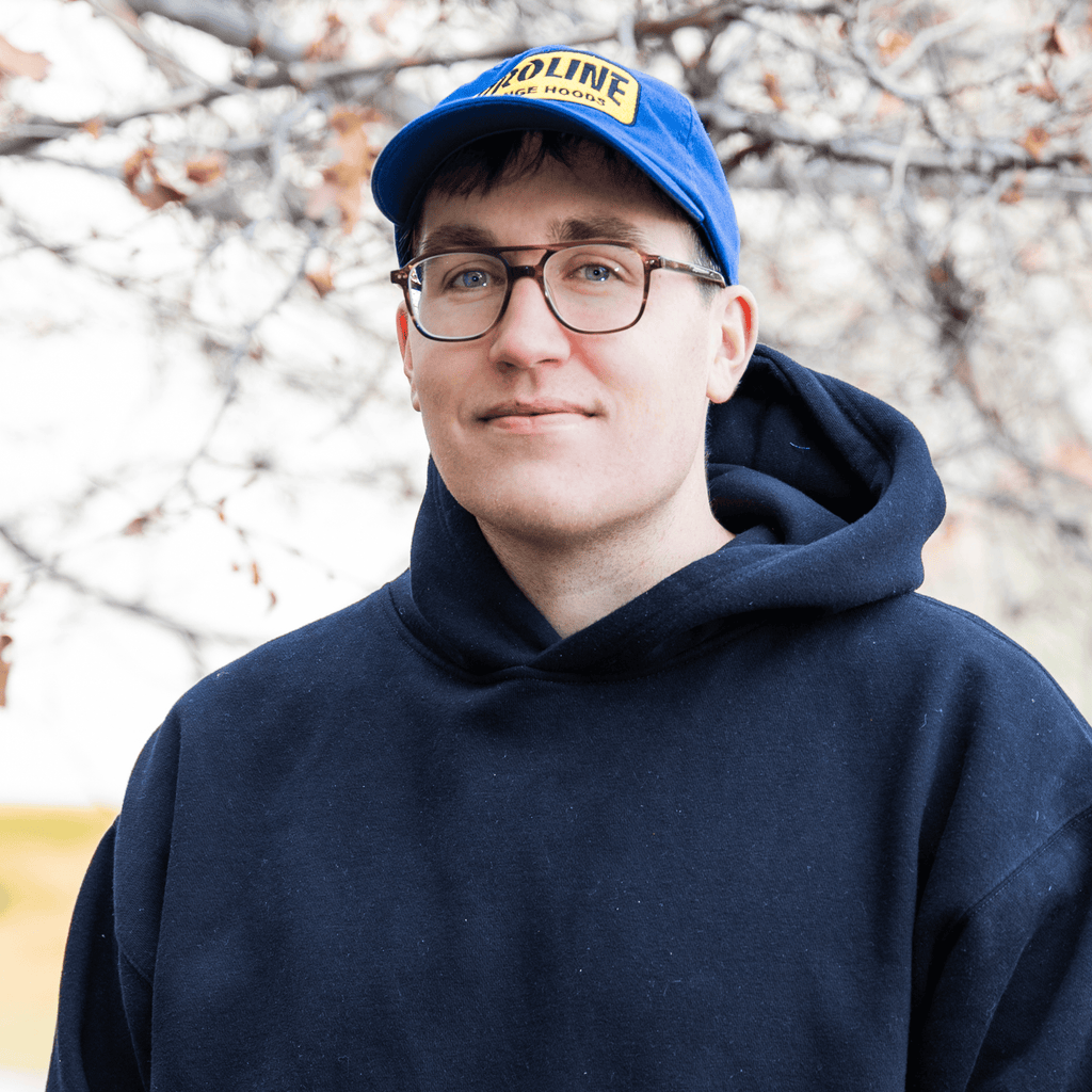 A person in glasses and a blue hoodie stands outside, blue cap on, tree branches behind. ProlineRangeHoods.com.