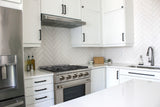 Modern white kitchen with Proline PLSR Gas Range (15,000 BTUs), herringbone backsplash, black handles. ProlineRangeHoods.com.