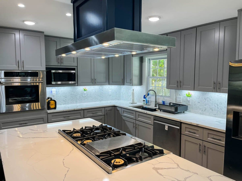 Modern kitchen—gray cabinets, marble counters, gas stove, stainless appliances, Proline Range Hood. ProlineRangeHoods.com.