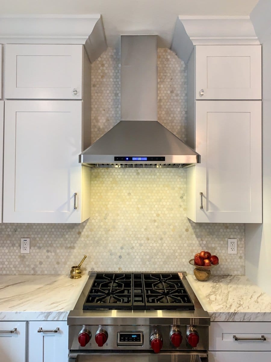 Modern kitchen with white cabinets, stainless steel stove, marble counters, apples, and ProlineRangeHoods.com PLFW 129 E range hood.