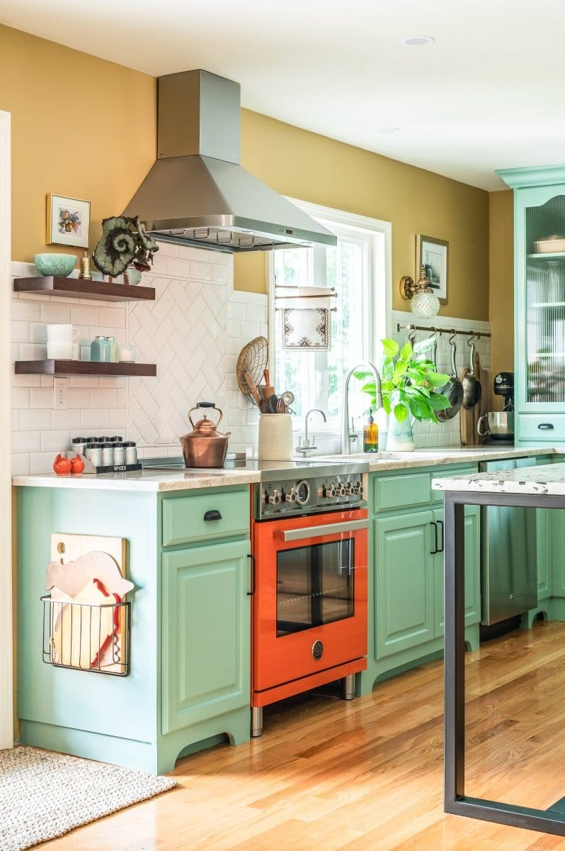 A vibrant kitchen features teal cabinets, an orange stove, and ProlineRangeHoods.com for sleek, efficient ventilation.