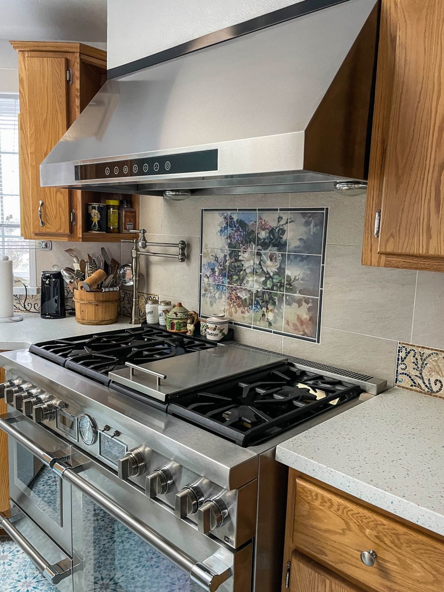 Contemporary kitchen with a stainless steel stove, ProlineRangeHoods.com PLJW 102 hood, wooden cabinets, and floral tiles.