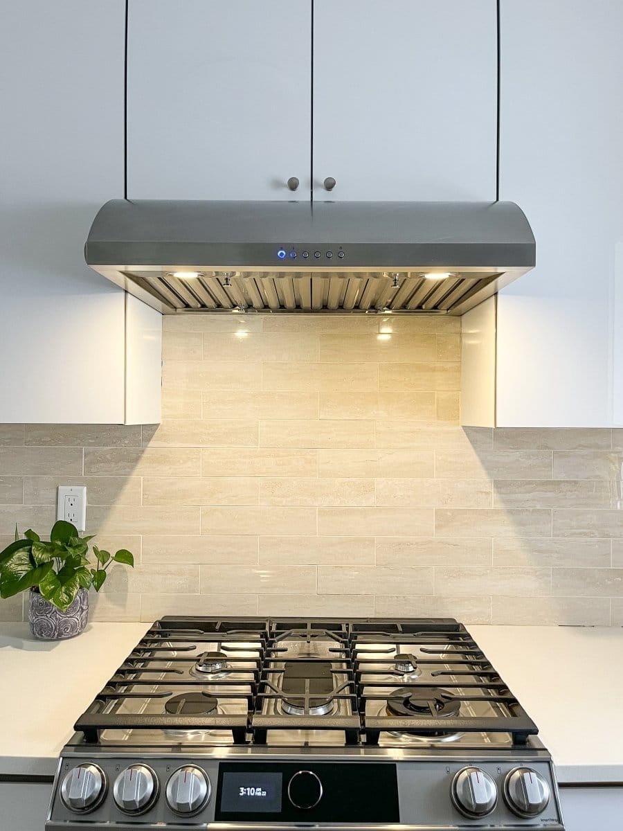 Modern kitchen with ProlineRangeHoods.com featuring PLJW 133 ductless 900 CFM hood, gas stove, white cabinets, and plant.