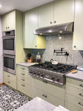 A modern kitchen with green cabinets features a ProlineRangeHoods.com hood in stainless steel, 900 CFM & ductless option.