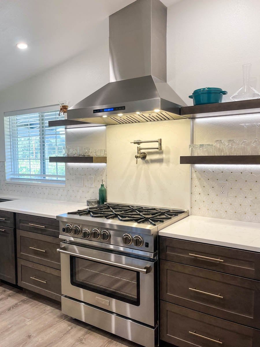Modern kitchen with stainless steel ProlineRangeHoods.com 1800 CFM Wall Range Hood, open shelves, & pot filler on tile wall.